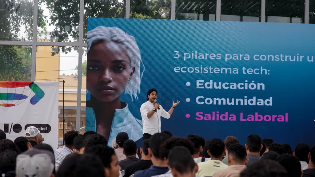 Charla ante una audiencia con la lámina de los tres pilares: educación, comunidad y salida laboral.